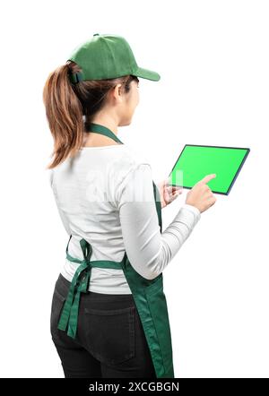 Asiatische Verkäufer tragen grüne Schürze und grüne Kappe lächelnd mit der Hand, die ein digitales Tablet mit leerem Bildschirm auf weiß hält Stockfoto