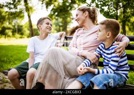 Glückliche Mutter sitzt mit ihren Söhnen auf der Bank im Park. Sie haben Spaß zusammen. Stockfoto