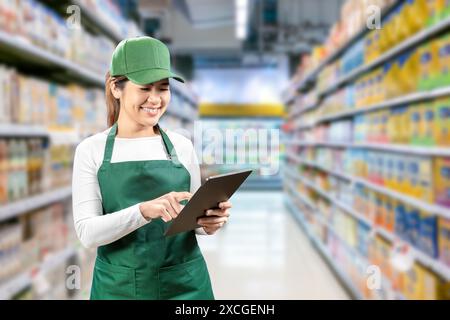 Asiatische Verkäufer tragen grüne Schürze und grüne Kappe lächelnd im Einzelhandel mit einem digitalen Tablet Stockfoto