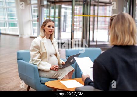 Schwangere reife Frau in weißem Anzug bei Geschäftstreffen mit Kollegen in einem modernen Büro oder Coworking Center. Professionelle Geschäftsfrau Multit Stockfoto