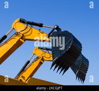 Schaufel und Hydraulikarm eines Baggers, isoliert auf klarem blauem Himmel Hintergrund, perspektivische Aufnahme aus flachem Winkel. Stockfoto