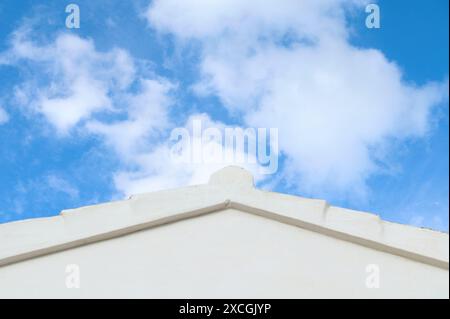 Weißes Dach des Gebäudes mit einem klaren blauen Himmel und flauschigen Wolken im Hintergrund, die Einfachheit und Ruhe darstellen. Stockfoto