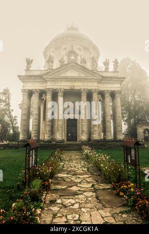 Nebelansicht der römisch-katholischen Kirche Exaltation of the Holy and St. Joseph in der Nähe des Dorfes Pidhirtsi, Lemberg, Ukraine. Alte Kirche am Hinterhof bei Sonnenaufgang Stockfoto