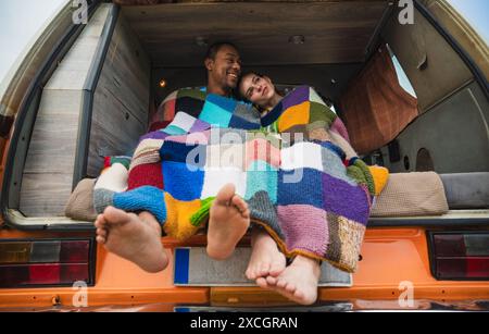 Glückliches, vielfältiges Paar, das bei Tageslicht in einem geparkten Van sitzt Stockfoto