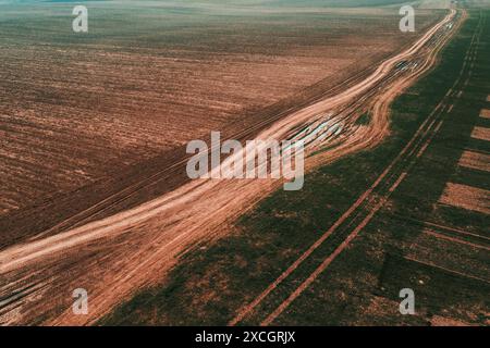 Luftaufnahme der kurvenreichen Feldstraße zwischen zwei landwirtschaftlichen Feldern, pov-Hochwinkelansicht der Drohne Stockfoto