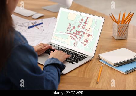 Frau arbeitet mit Katasterkarte auf Laptop am Tisch im Büro, Nahaufnahme Stockfoto