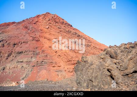 Ein Blick auf einen vulkanischen Berg mit roten und braunen Felsformationen unter einem klaren blauen Himmel auf den Kanarischen Inseln. Stockfoto