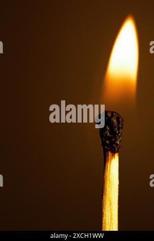 Makroaufnahme eines brennenden Streichholzstifts vor schwarzem Hintergrund mit schönen gelben und orangen Flammen. Stockfoto