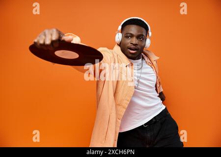 Eleganter schwarzer Mann mit Kopfhörern, die eine Aufnahme auf orangefarbenem Hintergrund halten. Stockfoto