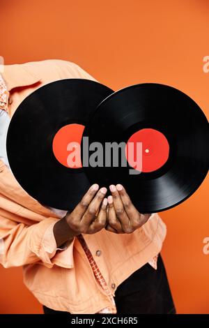 Schöner afroamerikanischer Mann, der zwei Schallplatten vor orangem Hintergrund hält. Stockfoto