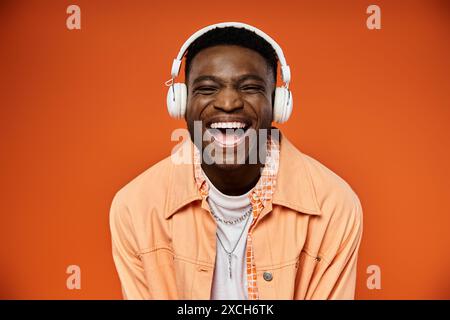 Ein eleganter schwarzer Mann lächelt mit Kopfhörern auf orangefarbenem Hintergrund. Stockfoto