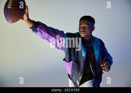 Junger afroamerikanischer Mann in stylischer lila Jacke hält einen Fußball. Stockfoto