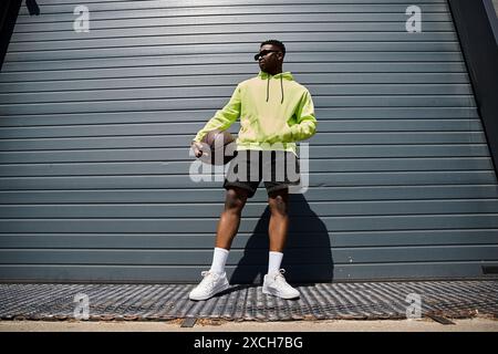 Junger afroamerikanischer Mann in gelbem Hoodie hält spielerisch Basketball. Stockfoto