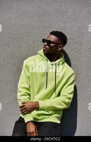 Hübscher afroamerikanischer Mann lehnt sich in einem hellgrünen Hoodie an eine Wand. Stockfoto