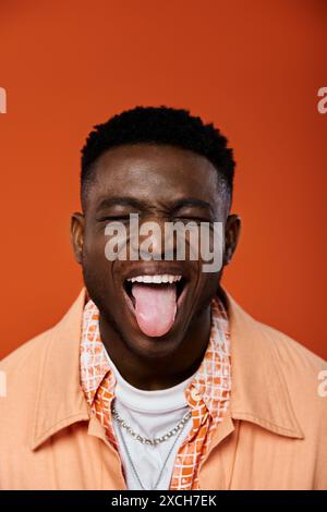 Ein gutaussehender afroamerikanischer Mann streckt spielerisch seine Zunge vor einem leuchtenden orangen Hintergrund aus. Stockfoto