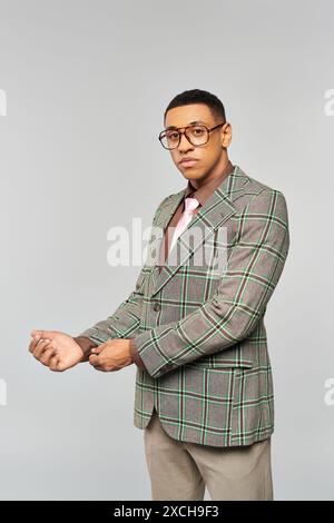 Ein Mann mit Brille posiert selbstbewusst in einem stylischen karierten Blazer. Stockfoto