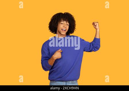 Selbstbewusster junger Mann, der seinen Bicep vor gelbem Hintergrund biegt Stockfoto