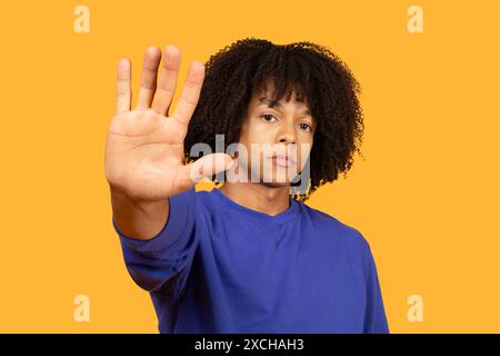 Junger Mann Mit Lockigem Haar, Der Die Hand Gegen Gelb Hält Stockfoto