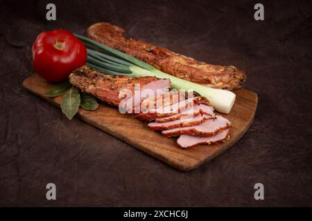 Schweinefilet Pastrami geräuchert und gewürzt, mit dünnen Scheiben, Tomaten und Frühlingszwiebeln, auf einem Holzschneidebrett, isoliert auf weiß Stockfoto