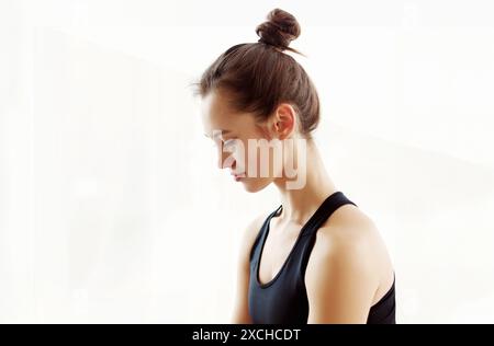 Junge Frau, die morgens drinnen meditiert, mit Haaren in Bun Stockfoto