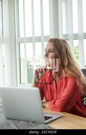 Eine attraktive Telearbeiterin Mitte der 40er-Jahre, die von zu Hause aus mit tiefem Fokus arbeiten kann. Im modernen Zeitalter ist Arbeit von überall möglich Stockfoto