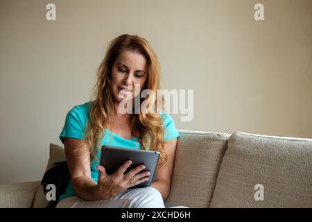 Ein intelligenter, lächelnder Remote-Mitarbeiter nutzt ein mobiles Tablet, um zu Hause eine intensive Arbeit zu erledigen. Stockfoto