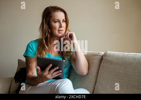 Ein intelligenter, lächelnder Remote-Mitarbeiter nutzt ein mobiles Tablet, um zu Hause eine intensive Arbeit zu erledigen. Stockfoto