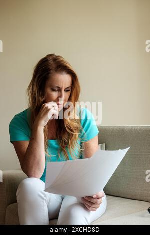 Eine Frau in ihren frühen 40ern hat mit viel Papierkram, Geldsorgen und dem Stress und der Sorge um unbezahlte Schulden zu kämpfen. Lebenshaltungskosten Krisenbild Stockfoto