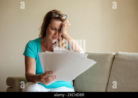 Eine Frau in ihren frühen 40ern hat mit viel Papierkram, Geldsorgen und dem Stress und der Sorge um unbezahlte Schulden zu kämpfen. Lebenshaltungskosten Krisenbild Stockfoto