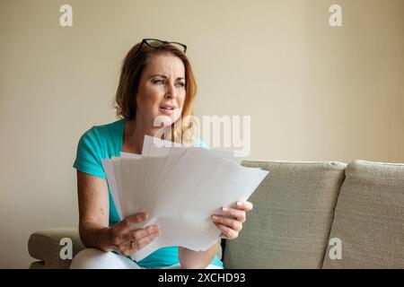 Eine Frau in ihren frühen 40ern hat mit viel Papierkram, Geldsorgen und dem Stress und der Sorge um unbezahlte Schulden zu kämpfen. Lebenshaltungskosten Krisenbild Stockfoto