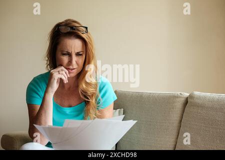 Eine Frau in ihren frühen 40ern hat mit viel Papierkram, Geldsorgen und dem Stress und der Sorge um unbezahlte Schulden zu kämpfen. Lebenshaltungskosten Krisenbild Stockfoto