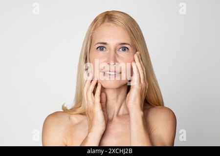 Nahaufnahme Porträt einer Frau, die ihr Gesicht gegen weiß berührt Stockfoto