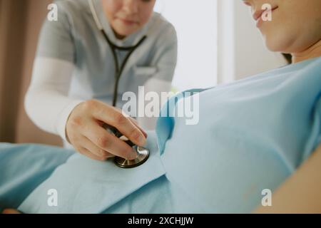 Mittlere Nahaufnahme von Geburtshelfern mit Stethoskop am Bauch der schwangeren Frau Stockfoto