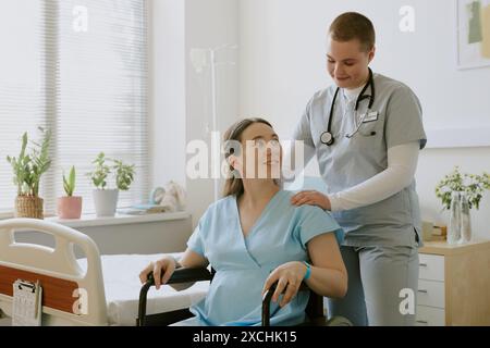 Schwester tröstet schwangere Patientin, während sie im Rollstuhl sitzt und sich auf die Geburt vorbereitet Stockfoto