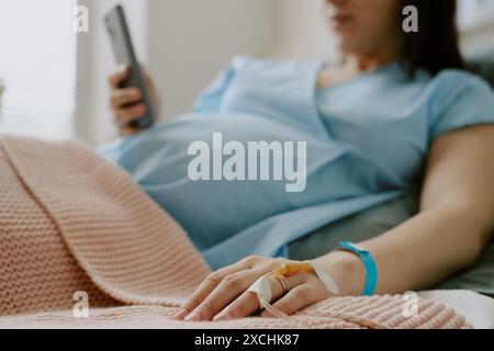 Mittlere Nahaufnahme einer der Frauenhände mit Tropfer und goldenem Ehering am Finger, die andere Hand hält das Smartphone Stockfoto