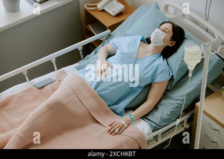 Weibliche Patientin streichelt ihren schwangeren Bauch, während sie Tropfer auf der Geburtsstation hat Stockfoto
