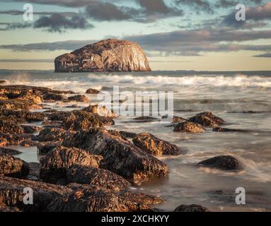 Langbelichtungsbild des Bass Rock, Schottlands Ostküste, von einem felsigen Ufer aus, an dem die Sonne auf brechenden Wellen scheint Stockfoto