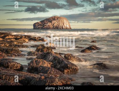 Blick auf Bass Rock, Schottlands Ostküste, von einem felsigen Ufer mit Sonne auf brechenden Wellen. Lange Belichtung Stockfoto