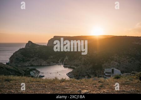 Ein wunderschöner Sonnenuntergang über einem Berg mit einer kleinen Stadt in der Ferne. Die Sonne untergeht hinter den Bergen und strahlt ein warmes Licht über die Landschaft. Stockfoto