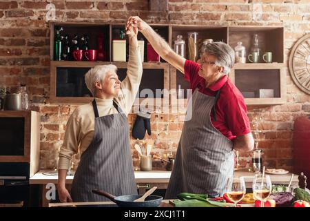 Seniorenpaar tanzt in der Küche mit Rotweingläsern Stockfoto