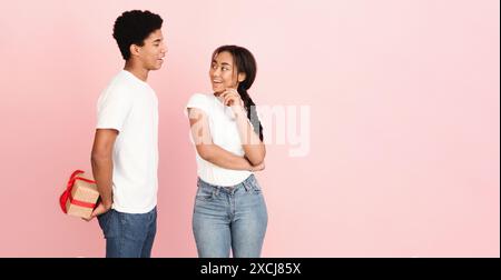 Junge Paare tauschen Geschenke gegen rosa Hintergrund bei Tageslicht aus Stockfoto