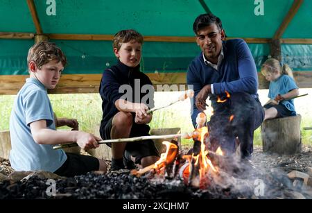 Premierminister Rishi Sunak toast Brot am offenen Feuer mit Kindern während eines Besuchs im Great Wood Farm Early Years Centre in Grantham in East Midlands, während er sich auf dem Wahlkampfpfad der General Election befindet. Bilddatum: Montag, 17. Juni 2024. Stockfoto