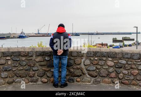 Ein Mann steht und sieht die Schiffe in einer Hafenstadt am Meer an. Bornholm Island, Ronne, Dänemark. Stockfoto