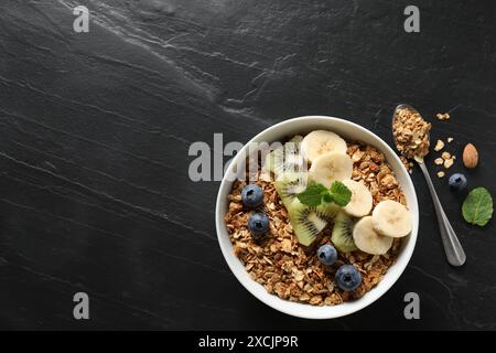 Leckeres Müsli mit Früchten und Beeren auf schwarzem Tisch, flach gelegen. Leerzeichen für Text Stockfoto