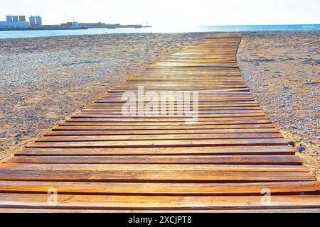 Holzsteg an einem Sandstrand, der in Richtung des ruhigen Meerwassers führt Stockfoto