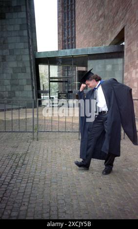 1970er Jahre, vor dem Eingang einer Kirche, posierte ein junger Mann in akademischen Insignien, langem Kleid und Mörtelbrett, während er den Abschluss der Universität feiert. Stockfoto