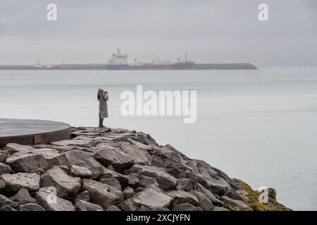 Junge Touristenfrau, die Fotos vom Meer vor Reykjavik von den Uferfelsen in Island macht Stockfoto