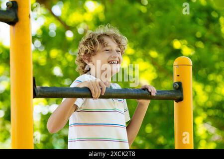 Kind auf dem Spielplatz. Aktives Kind, das auf dem Schulhof trainiert. Kinder spielen und klettern. Kleiner Junge auf Affenriegeln. Kinder haben Spaß an sonnigen Sommertagen Stockfoto