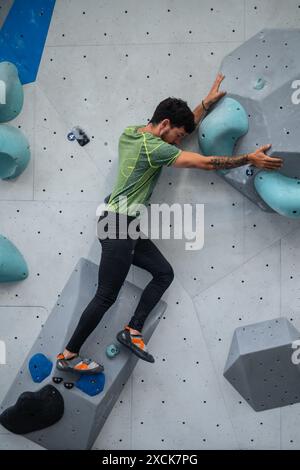 Junger Mann in seinen Zwanzigern, der drinnen auf eine Kletterwand klettert Stockfoto