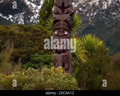 Detaillierte Nahaufnahme der typischen traditionellen Pou Whenua Holzpfahl Whakairo Schnitzereien aus der Maori-Kultur mit Pflanzen Hintergrund bei Dawson Falls Taranaki No Stockfoto